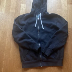 Svart hoodie från Polo Ralph Lauren - Säljer en klassisk svart hoodie från Polo Ralph Lauren med dragkedja och huva. Tröjan har långa ärmar och snören vid huvan för justering. Perfekt för en avslappnad stil.