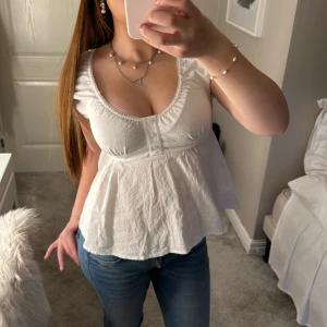 Vit blus med volangdetaljer - Säljer en söt vit blus med volangdetaljer och korta ärmar! Inga defekter och bra skick!