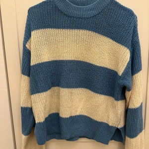 Randig stickad tröja från Gina Tricot - Säljer en mysig stickad tröja från Gina Tricot i blått och off-white. Tröjan har ett randigt mönster och långa ärmar, perfekt för kyligare dagar. Den är både stilren och bekväm. Det är en liten fläck på magen men går nog bort i tvätten!💕🤗