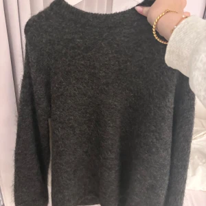 Mörkgrå stickad tröja - Mysig mörkgrå stickad tröja med rund halsringning och långa ärmar. Perfekt för kyliga dagar och ger en stilren look.