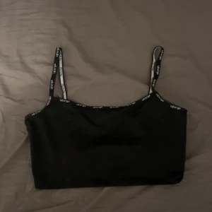 Svart linnetopp från Levi's - Snygg svart linnetopp från Levi's med smala axelband och logotyp längs kanterna. Aldrig använd 💕