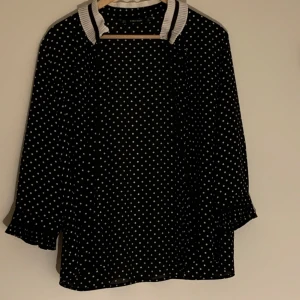 Svart prickig blus från Zara Basic - Snygg svart blus med vita prickar från Zara Basic. Blusen har trekvartsärmar och en stilren krage med volangdetaljer. Den har även knappar. Priset går att diskutera vid snabb affär. Kontakta gärna vid frågor och funderingar 
