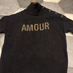 Zadig & Voltaire tröja - Säljer en snygg svart polotröja från Zadig & Voltaire med texten 'AMOUR! Tröjan går att knäppa upp vid halsen om man inte vill ha den hög❣️ sälj pågrund av att den inte används❣️pris går att diskuteras! Knappt använd och ser mycket nopprigare ut på bilden en vad den är. Nypris 1300❤️OBS den är nopprig, men går att ta bort!