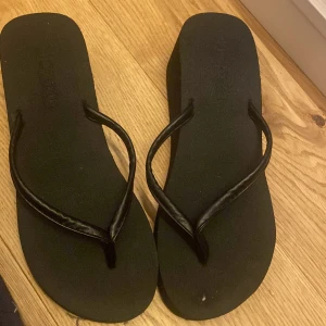 Svarta flip-flops med kilklack - Snygga svarta flip-flops med kilklack, perfekta för sommardagar. De har en enkel design med smala remmar och en bekväm sula. Passar bra till både strand och stadspromenader. Aldrig använda, endast testade men pris kan gärna diskuteras🤩