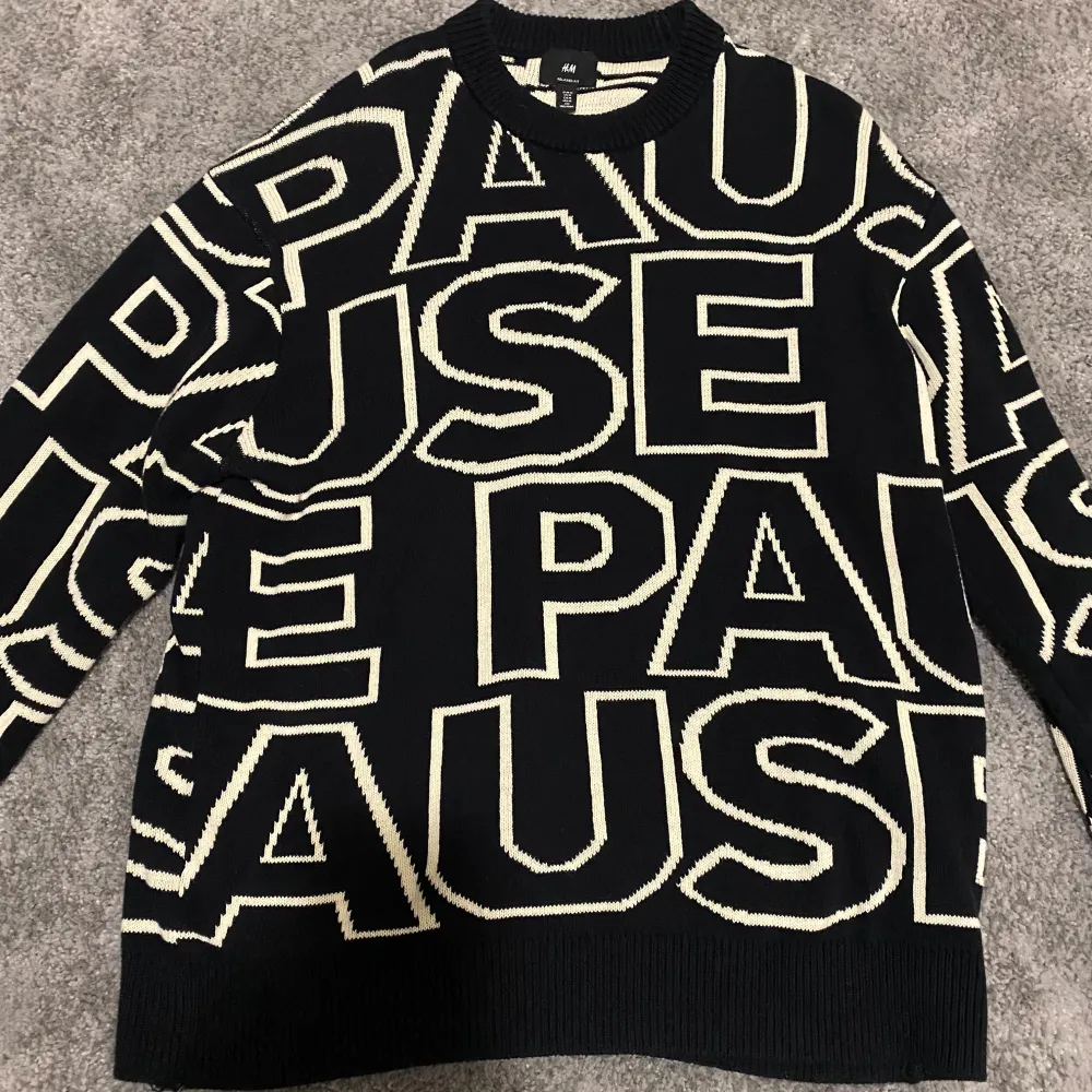 Säljer en svart tröja från H&M med stora vita bokstäver som bildar ordet 'PAUSE'. Tröjan har en avslappnad passform och långa ärmar. Perfekt för en cool och avslappnad stil. Kan kännas lite som oversize!. Neuletakit & Villapaidat.