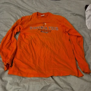 Orange långärmad tröja från Champion - Säljer en orange långärmad tröja från Champion med trycket 'Virginia Tech Athletics Hokies' på framsidan. Perfekt för dig som gillar sportig stil och vill visa ditt stöd för Virginia Tech. har en bekväm passform.