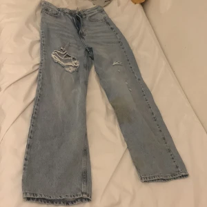 Ljusblå jeans från &Denim - Säljer ett par ljusblå jeans från &Denim med en loose straight passform och hög midja. Byxorna har slitningar och är ankel-långa, vilket ger en trendig look. Perfekta för en avslappnad stil. De har dock några små fläckar men det går nog bort i tvätten.