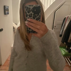 Grå kofta - Säljer en mysig grå kofta med knappar framtill. Koftan har långa ärmar och en croppad passform, perfekt för kyligare dagar.