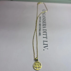 Guldhalsband med livets träd från ur & Penn  - Elegant guldhalsband med ett hänge i form av livets träd. Kedjan är tunn och smidig, vilket ger en stilren look. Perfekt för att lägga till en touch av symbolik och elegans till din outfit. Aldrig använd. Säljer för 70 kronor.✨