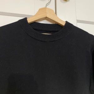 Stickad svart tröja från Bertoni - Säljer en stilren svart tröja från Bertoni. Tröjan har en klassisk rund halsringning med ribbade kanter. Perfekt för en minimalistisk look.