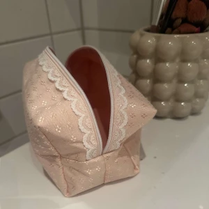 Rosa necessär med spetsdetaljer - Söt rosa necessär med dragkedja och fina spetsdetaljer. Perfekt för att förvara smink eller andra småsaker. Den har en praktisk form och är lätt att ta med sig💗💗