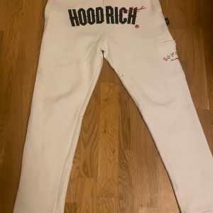 Vita mjukisbyxor från Hoodrich - Säljer ett par vita mjukisbyxor från Hoodrich med tryck i svart och rött. Byxorna har en avslappnad passform och en elastisk midja. Perfekta för en bekväm och stilren look.