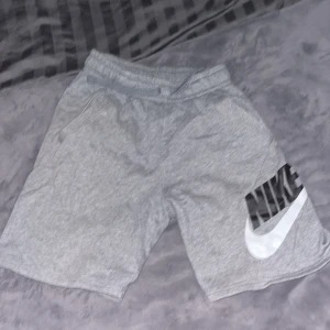 Grå shorts från Nike - Snygga grå shorts från Nike med en stor vit logga på benet. Perfekta för en avslappnad stil eller träning. De har en elastisk midja för extra komfort. Inga defekter!