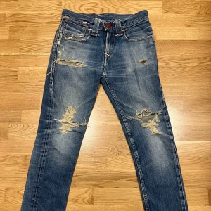 Blå slitna jeans från Levi's - Säljer ett par blå vintage levis jeans med en sliten look. De har raka ben och coola detaljer som en röd knapp fram vita broderingar. Skitcoola tycker jag iallafall och jag hoppas verkligen att nån kan älska dem lika mycket som jag gjort