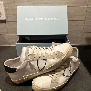Vita sneakers från Philippe Model - Snygga vita sneakers från Philippe Model med svarta detaljer och snörning. Skorna har en klassisk design med en vit sula och en diskret logotyp på sidan. Perfekta för en stilren look. Allt og ingår. 