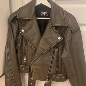 Olivgrön skinnjacka från Zara - Snygg olivgrön skinnjacka från Zara med coola dragkedjedetaljer och bälte i midjan. Använd en gång mycket bra skick 