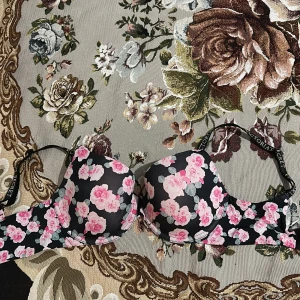 Blommig bh från Victoria's Secret - Säljer en snygg bh från Victoria's Secret med ett blommigt mönster i rosa och vitt på en svart bakgrund. Bh:n har justerbara axelband och en bekväm passform. Har klippet storlek och skötsel lappar 