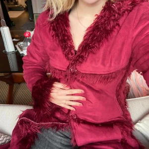 Vinröd pälskappa💓 - Säljer en snygg vintöd kappa från Duban med fluffiga pälsdetaljer längs kragen och ärmsluten. Jackan har en lång passform och knäpps med knappar framtill.💓💓