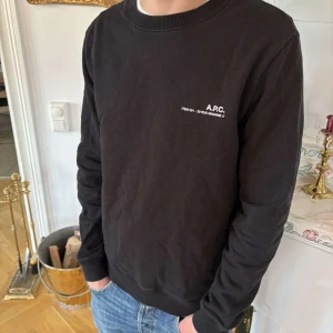 Svart tröja från A.P.C. - Säljer en stilren svart tröja från  A.P.C. med vit textdetalj på bröstet. Perfekt för en minimalistisk look.