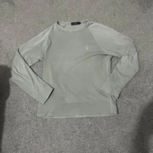 Grå tröja från Polo Ralph Lauren - Säljer en stilren grå tröja från Polo Ralph Lauren med det klassiska broderade logotypen på bröstet. Tröjan har långa ärmar och en bekväm passform. Perfekt för en avslappnad look.