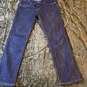 Blå jeans från Oly One - Snygga blå jeans från Oly One med rosa knappar och kontrastsömmar. Klassisk femficksdesign och rak passform. Perfekta för en avslappnad stil.