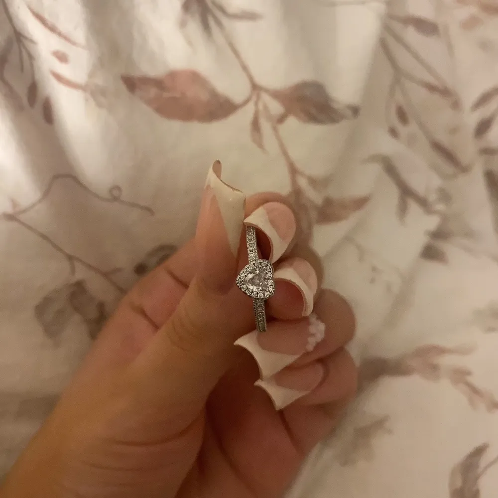 Elegant Pandora liknande silverring med en glittrande hjärtformad sten i mitten, omgiven av små gnistrande stenar. Perfekt för speciella tillfällen eller som en kärleksfull gåva. Storleken kan justeras💞Helt ny priset kan diskuteras. Asusteet.