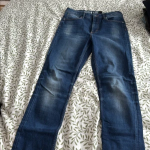 Blå jeansbyxor - Snygga blå jeansbyxor med klassisk femficksdesign och en läderdetalj vid midjan. De har en straight passform och är perfekta för en avslappnad stil. Byxorna har en lätt tvättad look som ger dem en cool och trendig känsla.