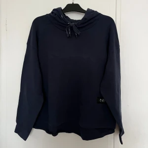 Mörkblå hoodie från New Apparel - Säljer en mörkblå hoodie från New Apparel i storlek XL. Liten i storlek så passar även M. Den har en justerbar huva med snören och en liten logga på framsidan. Perfekt för en avslappnad stil och för träning ❤️