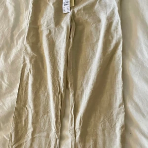 Beige linnebyxor från Gina tricot - Snygga beige linnebyxor perfekta för varma dagar. De har en avslappnad passform och är tillverkade i ett lätt och luftigt material. Byxorna har en enkel design som gör dem lätta att matcha med olika toppar.