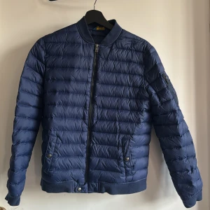 Blå quiltad jacka från Polo Ralph Lauren - Säljer en snygg blå quiltad jacka från Polo Ralph Lauren. Jackan har en dragkedja framtill och ribbade muddar. Den är långärmad med en praktisk ficka på ärmen och två fickor med knappar framtill. Perfekt för kyligare dagar! Passar stl 160-164