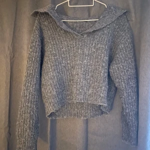 Grå stickad tröja - Säljer en grå stickad tröja med ribbad struktur. Tröjan har långa ärmar och en bred krage från Gina Tricot.
