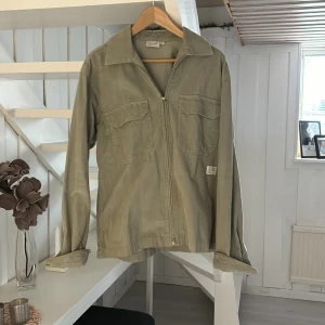 Grön manchesterjacka med dragkedja - Säljer en stilren grön manchesterjacka med dragkedja och två bröstfickor. Jackan har en klassisk krage och långa ärmar, perfekt för en avslappnad look. Passar bra till jeans och sneakers.