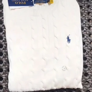 Vit stickad tröja från Ralph Lauren - Säljer en stilren vit stickad tröja från Ralph Lauren med det klassiska broderade logotypen i blått. Tröjan har en kabelstickad design och rund halsringning. Perfekt för en elegant och avslappnad look.