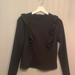 Mörk grön blus med volang från Zara - Elegant mörk grön blus från Zara med långa ärmar och dekorativa volanger framtill och baktill.  Perfekt för en stilren look. 