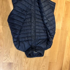 Svart dunjacka från Gant - Snygg svart dunjacka från Gant med dragkedja och knappar. Perfekt för kyligare dagar och enkel att matcha med andra plagg. Jackan har en stilren design med praktiska fickor.