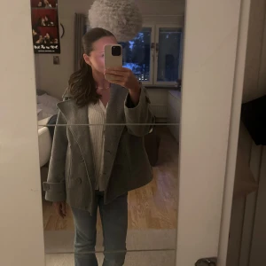 Grå kappa från design by si - Säljer en stilren grå kappa med knappar framtill. Jackan har en klassisk design med bred krage och långa ärmar. Perfekt för kyligare dagar och ger en elegant touch till din outfit. Storlek xs/s