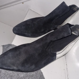 Svarta boots med silverdetaljer - Snygga svarta boots i mocka med spetsig tå och silverdetaljer runt hälen. Perfekta för en stilren look. De har en elastisk panel för enkel på- och avtagning.