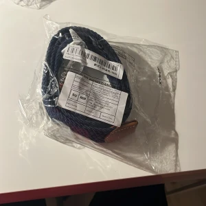 Blått flätat bälte -  Helt nytt Snyggt blått flätat bälte med bruna skinn-detaljer. Perfekt för att ge en stilren touch till din outfit. Bältet är i ett elastiskt material som ger en bekväm passform.