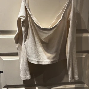 BIKBOK Vit ribbad offshoulder topp - Säljer en stilren vit ribbad offshoulder topp med långa ärmar. Perfekt för en trendig look. Passar bra till både jeans och kjol.