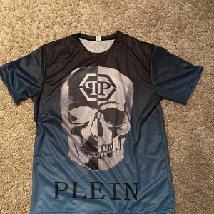 Philipp plein T-shirt - Cool  t-shirt från Plein med stort dödskalletryck på både fram- och baksida. Material påminner om tränings tröja.                                                                                       Har ingen philipp plein tag                                                        Sitter större i storleken 