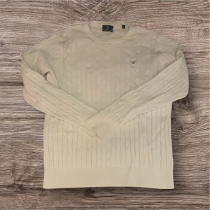 Vit stickad tröja från GANT - Säljer en stilren vit stickad tröja från GANT med kabelstickat mönster. Tröjan har långa ärmar och en rund halsringning. Perfekt för en klassisk och tidlös look.