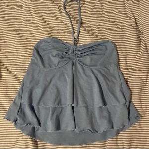 Blå halternecktopp - en supersöt blå halterneck topp med volangdetaljer. Toppen har en knytning runt halsen. storlek xs-s