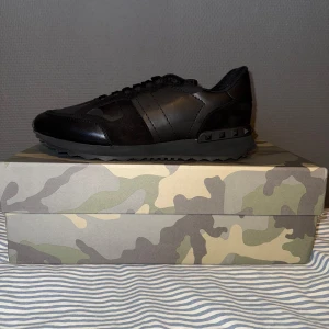 Svarta sneakers från Valentino Garavani - Snygga svarta sneakers från Valentino Garavani med en stilren design. Skorna har en diskret camouflage-mönster och är tillverkade i skinn. Perfekta för en trendig look. Helt nya.