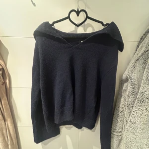 Mörkblå offshoulder tröja från Gina Tricot - Säljer en snygg mörkblå stickad tröja från Gina Tricot. Tröjan har en ribbad kant vid axlarna och är perfekt för en stilren look. Den är långärmad och gjord i ett mjukt material som håller dig varm.