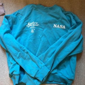 Turkos sweatshirt med NASA-tryck - Säljer en cool turkos sweatshirt med tryck från hm och texten 'Explore & Pioneer'. Tröjan har långa ärmar och ribbade muddar vid ärmslut och nederkant. Perfekt för rymdentusiaster! 🚀