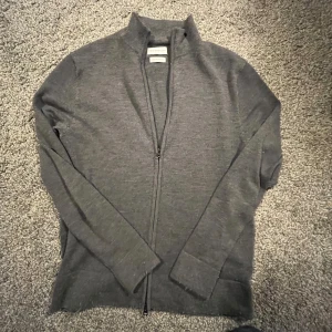 Grå merinoulltröja från These Glory Days - Säljer en stilren grå tröja i merinoull från These Glory Days. Tröjan är köpt helt ny och är max använd 3 gånger. Nypris ligger på 1100 kr. Mitt pris : 650. Tröjan har en dragkedja framtill och långa ärmar, perfekt för kyligare dagar. Den är mjuk och bekväm, idealisk för både vardag och mer uppklädda tillfällen. Pris kan diskuteras vid snabb affär. Hör av dig vid frågor. //Tom🍾