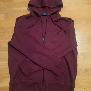 Vinröd hoodie från Polo Ralph Lauren - Säljer en snygg vinröd hoodie från Polo Ralph Lauren. Den har en dragkedja framtill och en klassisk huva med snörning. Perfekt för en avslappnad stil. 🧥