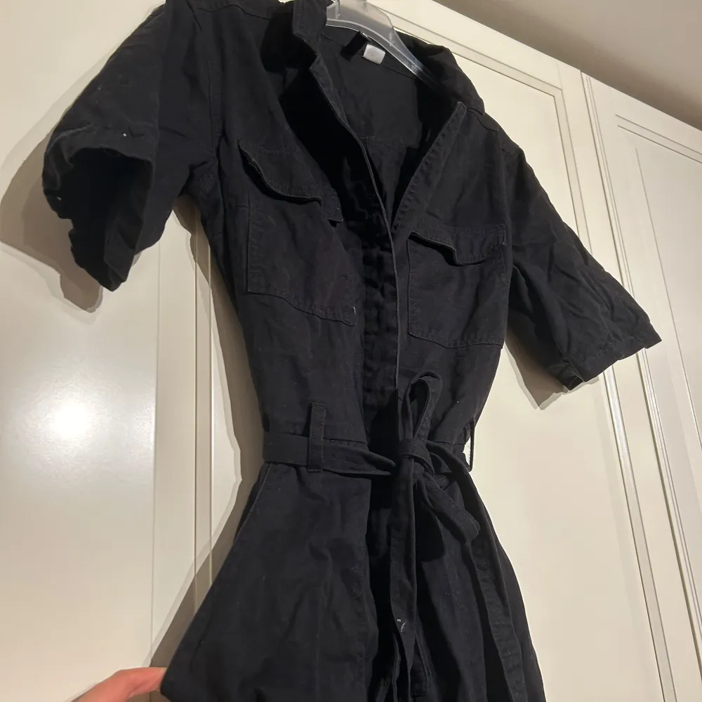 Säljer en svart jumpsuit i bra skick. Den har korta ärmar och ett knytband i midjan för en snygg passform. Materialet känns bekvämt och lätt att bära. . Jeans & Byxor.