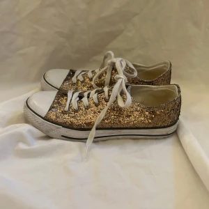 Glittriga sneakers från Mywear - Snygga glittriga sneakers från Mywear i guld med vita snören. Perfekta för att lysa upp vilken outfit som helst! De har en klassisk sneakerdesign med låg profil och är i  bra skick. Perfekta för festliga tillfällen eller när du bara vill känna dig extra glamorös.