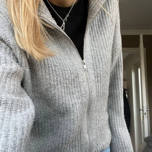 Grå stickad kofta med dragkedja - Mysig grå stickad kofta från BikBok med dragkedja framtill. Perfekt för kyliga dagar och passar till både jeans och kjol. Koftan har en ribbad struktur och långa ärmar. 